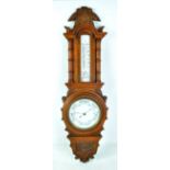 A thermometer and barometer combination in carved oak case, length 84cm.