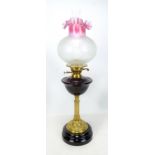 A late Victorian brass oil lamp with dark ruby red glass reservoir,