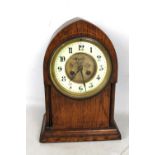 An oak cased lancet shaped mantel clock, the enamelled chapter ring set with Arabic numerals,
