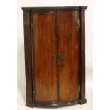 A 19th century oak bowfronted corner cupboard with twin doors enclosing two shelves.
