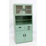 A green painted kitchenette of two glazed cupboard doors above shelf to upper section with three
