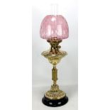 A brass oil lamp with duplex burner, cranberry shade and clear glass chimney on circular base,