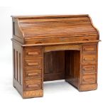 An early 20th century oak roll top desk with fitted interior above central drawer flanked by two