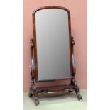 A Victorian mahogany cheval mirror with arched plate held by scrolling side supports capped with