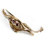 A yellow metal stylised floral brooch set with three purple coloured stones, stamped 9ct to reverse,
