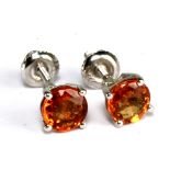 A pair of 18ct white gold and orange sapphire ear studs, each round cut stone in high claw