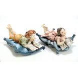 CAPODIMONTE; a pair of figures of children upon cushions reading, each length approx 20cm (2).