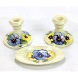 MOORCROFT; a pair of 'Pansy' pattern tubeline decorated squat candlesticks on pale green ground,