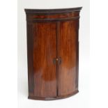 A 19th century mahogany bowfronted corner cupboard with dentil moulded cornice above twin doors