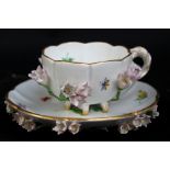 MEISSEN; an early 20th century floral encrusted and gilt heightened cup and saucer, with hand