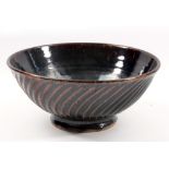 EDWARD HUGHES (1953-2006); a large fluted stoneware bowl covered in tenmoku breaking to khaki glaze,