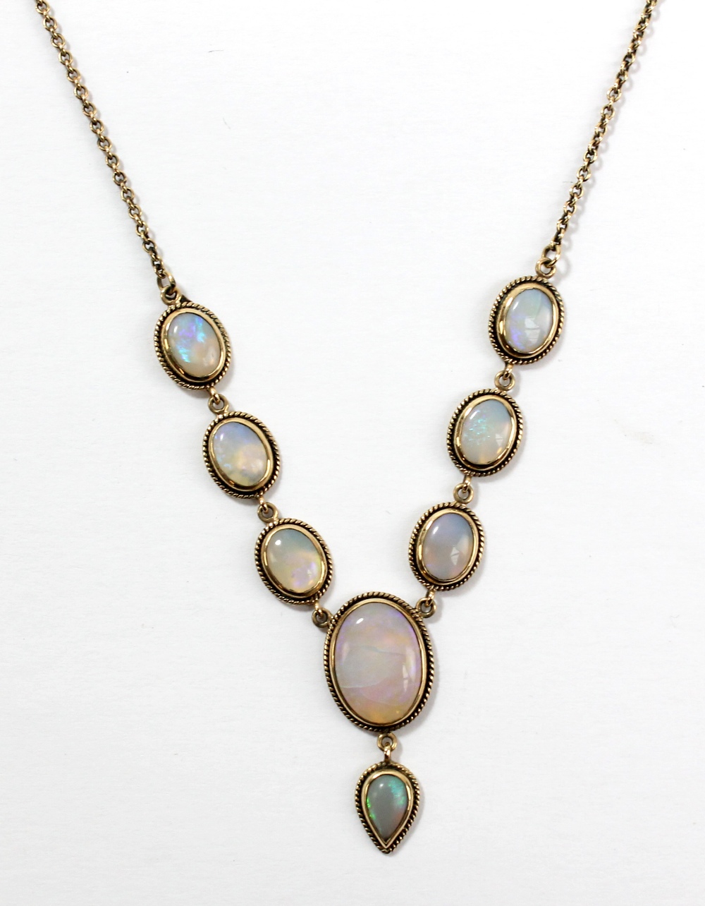 A yellow metal mounted opal pendant comprising seven oval cut stones and pear cut drop suspended