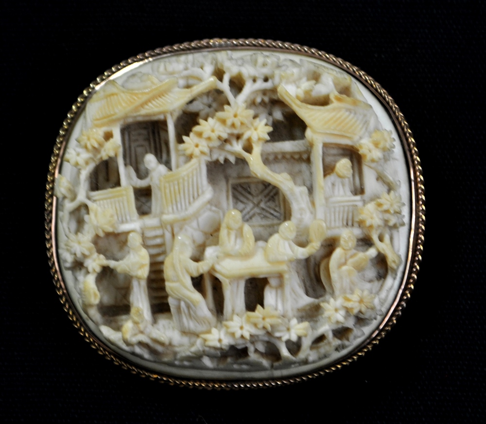 A late 19th/early 20th century Chinese Canton ivory brooch, heavily carved with figures in a garden,