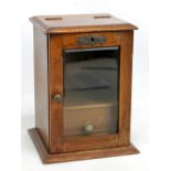 An Edwardian oak smoker's cabinet with hinged top above single glazed door enclosing pipe rack and