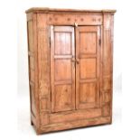 A Continental pine wardrobe, the twin doors flanked by fluted and reeded pilasters raised on stile