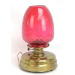 A brass circular oil lamp with cranberry tinted shade, height 45cm.