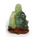 A Chinese carved mottled jade figure of seated laughing Buddha, raised on a shaped wooden base,