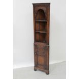 A narrow mid/late 20th century carved oak corner unit with shaped shelves over a cupboard door,