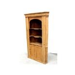 An early 20th century stripped pine corner unit with shaped shelves over single cupboard door,