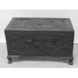 An ebonised Chinese camphorwood chest with relief carved decoration to four sides and the lid,