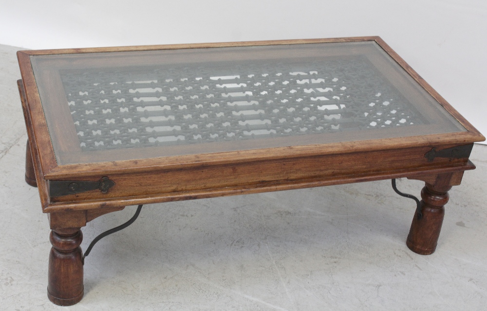 An Indonesian hardwood coffee table with wrought iron panel and a glass top supported on turned