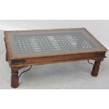 An Indonesian hardwood coffee table with wrought iron panel and a glass top supported on turned