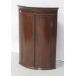 A 19th century mahogany bow-front inlaid wall-hanging corner cupboard with three interior shelves,