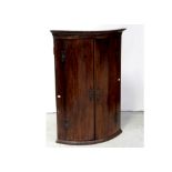 A George III mahogany bow-front corner cabinet with steel hinges and black painted interior shelves,