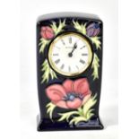 MOORCROFT; a floral tube line decorated clock on navy ground, the dial set with Roman numerals, WM