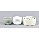 A straight sided porcelain vessel enclosing a set of five small beakers, one with handle,