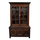A large oak bookcase, the upper section with twin glazed doors enclosing three shelves, the lower