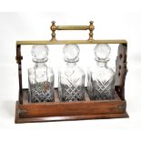 An Edwardian oak and brass mounted Betjemann's patent three bottle tantalus with reeded carrying