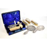 A cased five piece silver backed dressing table set with floral decoration, Birmingham 1904, and a