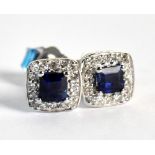 A pair of white metal diamond and sapphire ear studs, the princess cut sapphire surrounded by