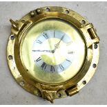 A brass ship's porthole, now converted into an electric wall clock, the silvered chapter ring set