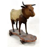 A late 19th/early 20th century hide covered cow on wooden stand with wheels, approx 25 x 27cm.