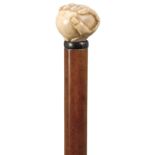 AN EARLY 20TH CENTURY WALKING CANE, the ivory handle carved as a fist holding a ball, malacca