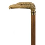 AN EARLY 20TH CENTURY WALKING CANE, the large ivory handle carved as the head of an eagle with glass