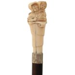 A LATE 19TH CENTURY WALKING CANE, the ivory handle carved as two children reading a book, slender