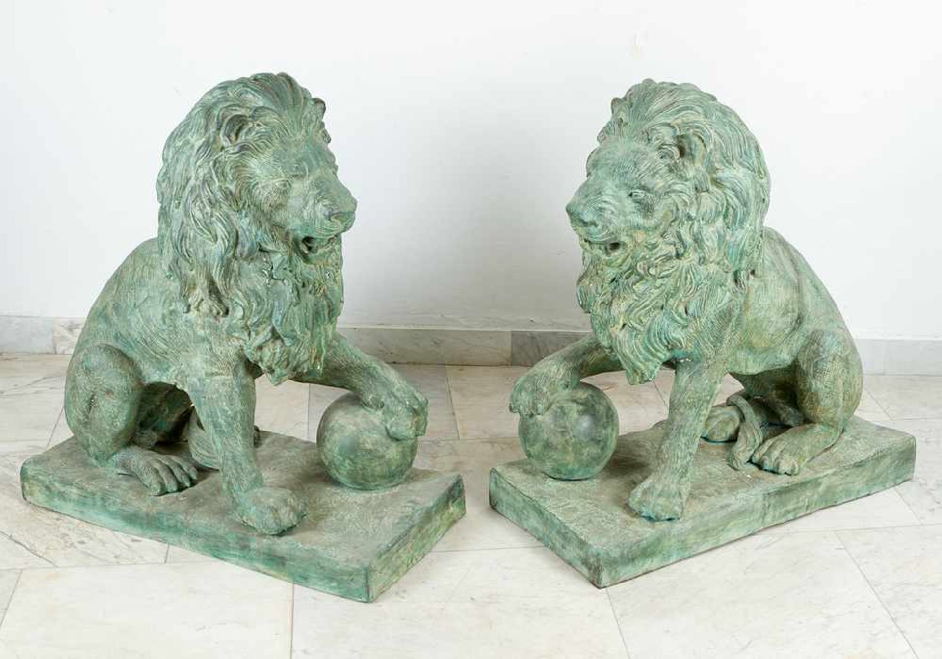 Pair of large bronze lions in sitting position with ball in paw on rectangular integrated bases.