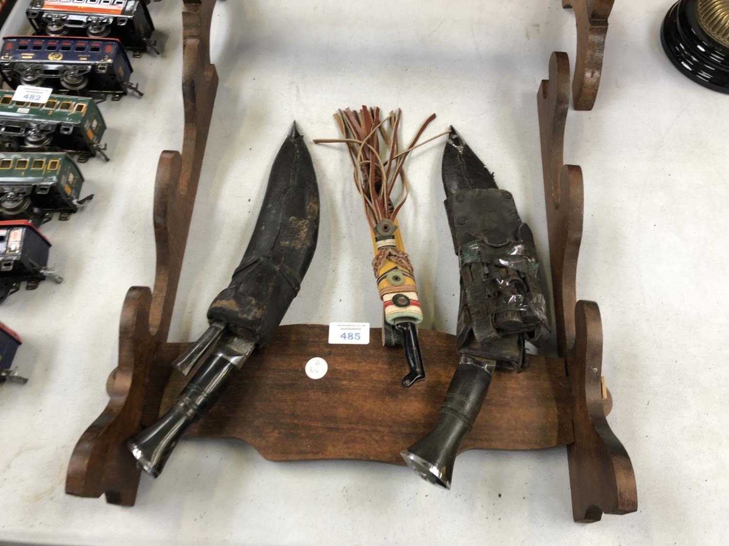 A WOODEN DISPLAY STAND WITH VARIOUS VINTAGE 'KUKRI' KNIVES ETC