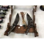 A WOODEN DISPLAY STAND WITH VARIOUS VINTAGE 'KUKRI' KNIVES ETC