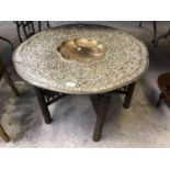 A MIDDLE EASTERN CARVED WOODEN COFFEE TABLE WITH BRASS CHARGER TOP, DIAMETER 77CM