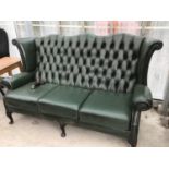 A GREEN LEATHER CHESTERFIELD HIGH BACKED WING BACK THREE SEATER SOFA