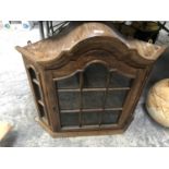 A WOODEN CORNER CUPBOARD WITH GLASS FRONTED DOOR