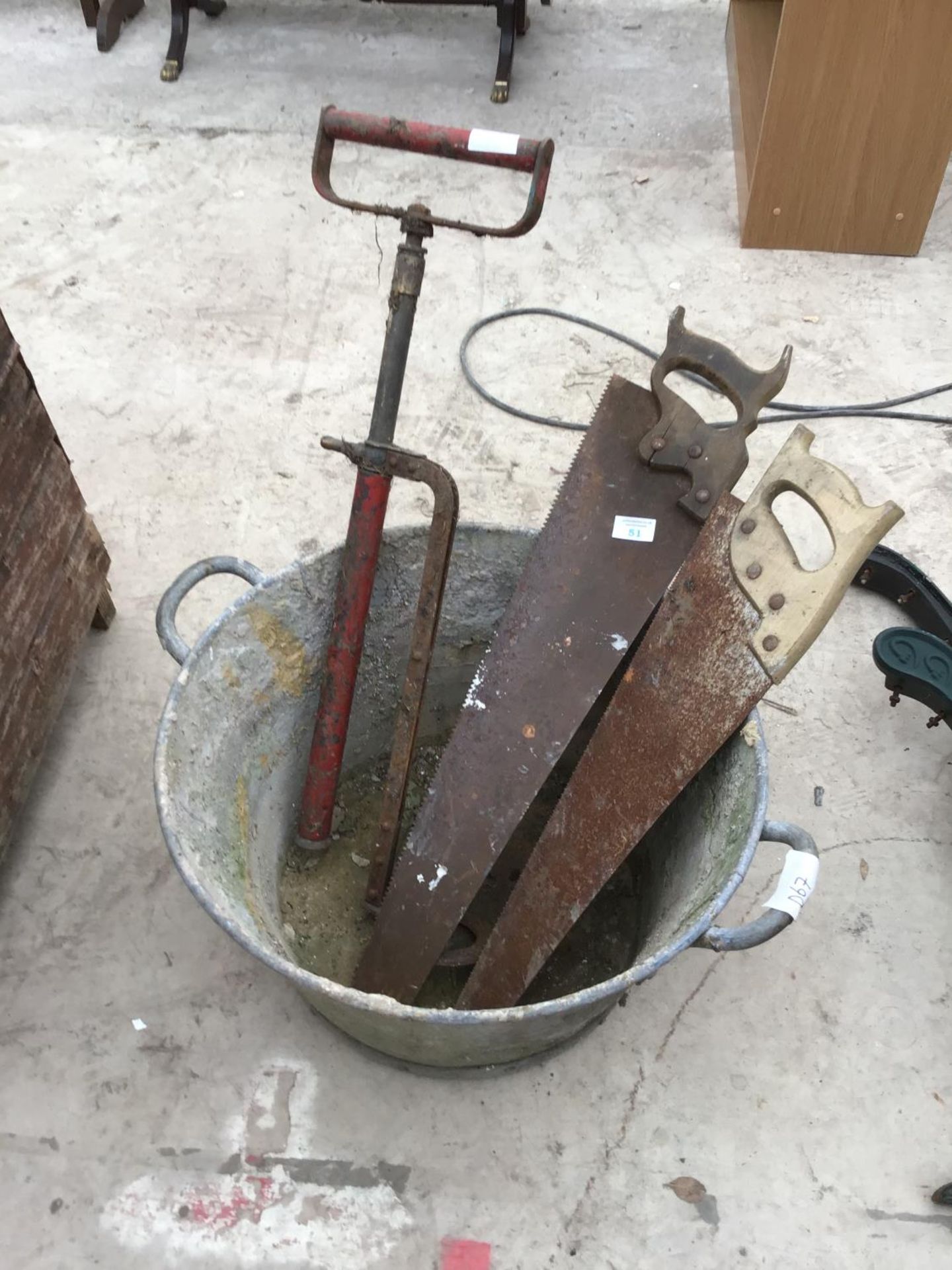 A GALVANISED TUB WITH A BARREL PUMP AND TWO SAWS