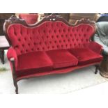A FRENCH STYLE CARVED WOODEN AND RED BUTTON BACK UPHOLSTERED THREE SEATER SOFA