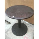 A ROUND WOODEN PUB STYLE TABLE ON A BLACK CAST IRON BASE