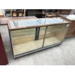 AN OAK FRAMED GLASS SHOP DISPLAY CABINET WITH MEASURING STICK AND INTERIOR GLASS SHELF