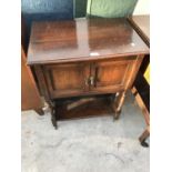 AN OAK TWO DOOR CABINET WITH LOWER SHELF ON CASTOR WHEELS